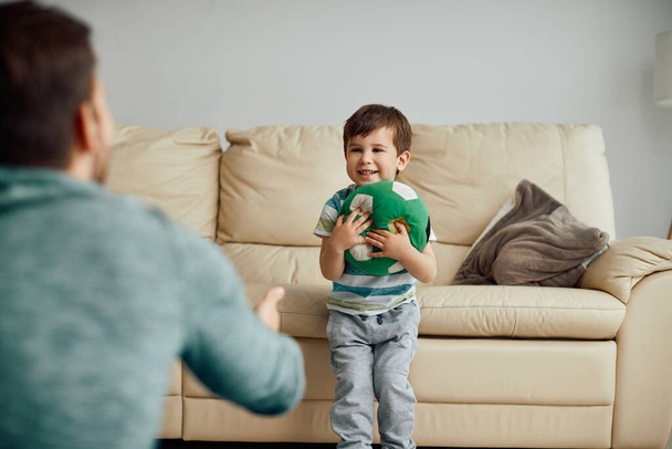 Happy kid and his father having fun while playing with a ball at home.  - 写真・画像