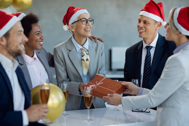 Šťastná zralá podnikatelka dostane vánoční dárek od svých spolupracovníků na párty v kanceláři. - Fotografie, Obrázek