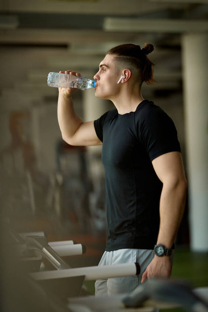 Fiatal sportoló, akinek víz szünet futás közben futópad egy edzőteremben.  - Fotó, kép