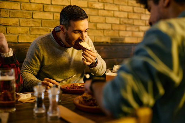 Young man eating while gathering with friends for lunch in a pub.  - Foto, imagen