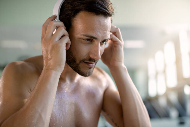 Young athletic man using headphones while listening music during sports training in a gym.  - Photo, image