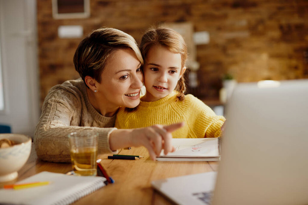 Щаслива мати показує щось на комп'ютері своїй маленькій доньці вдома
.  - Фото, зображення