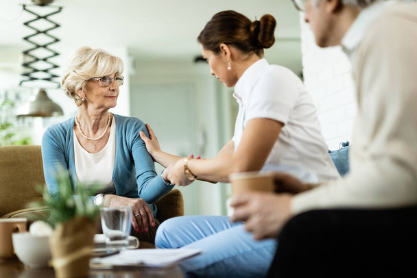 Female nurse communicating with senior woman while being in home visit. Focus is on senior woman.  - Photo, image