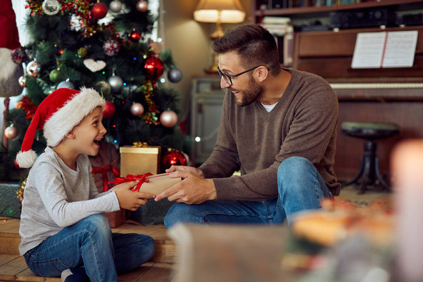Счастливый отец дарит своему сыну подарок в рождественское утро дома. - Фото, изображение