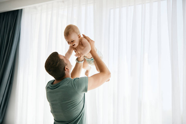 Playful father having fun with his baby boy while spending time together at home.  - 写真・画像