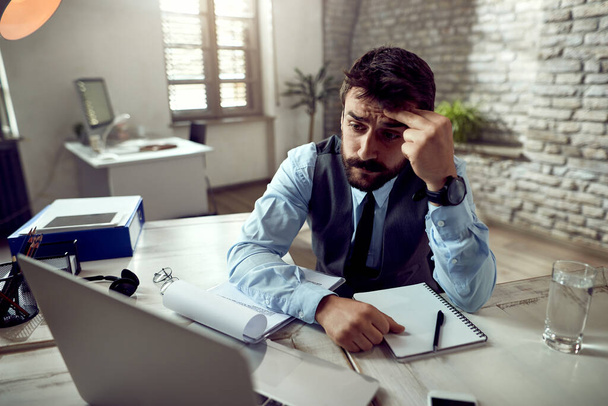Distraught businessman reading problematic e-mail on laptop while working in the office.  - Photo, Image