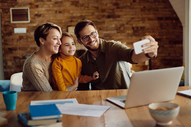 Happy parents with daughter using mobile phone and taking selfie at home.  - Fotoğraf, Görsel