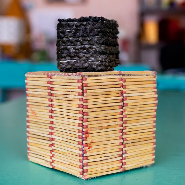 Two handmade cubes on a blurred background. A black cube made of threads stands on a cube made of matches - Φωτογραφία, εικόνα