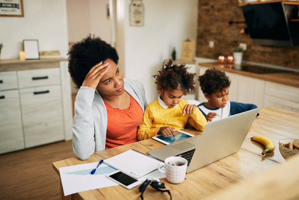 Pensive African American mother with two children feeling distressed about working from home. - Zdjęcie, obraz