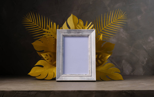empty white picture frame decorate with golden paper cut style elements of leaf on gray concrete wall background, copy space - Foto, imagen