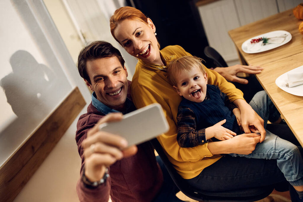 Happy parents and their son taking selfie and having fun in dining room.  - Фото, изображение