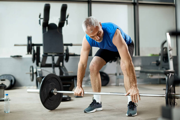 Mature sportsman exercises strength with barbell during gym work - Valokuva, kuva