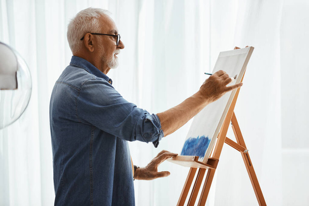 Старший художник додає фарбу під час картини на полотні у своїй студії
. - Фото, зображення