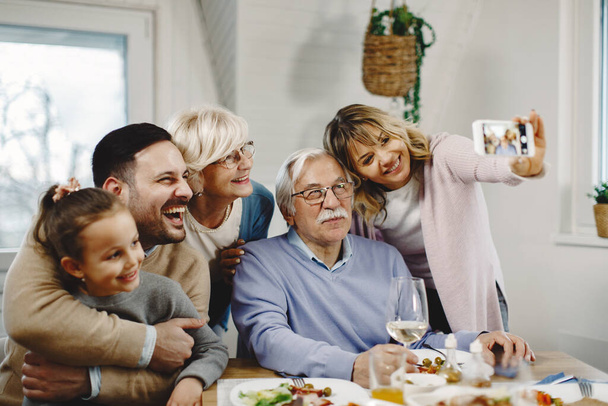 Cheerful extended family having fun while taking selfie with smart phone at dining table.  - 写真・画像