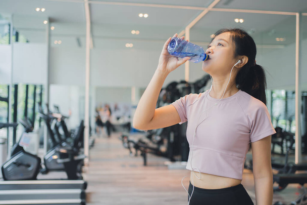 Asiatisch schön frau trinken wasser im die fitnessstudio nach training. - Foto, Bild
