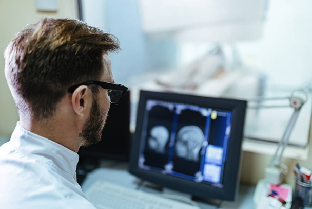 mężczyzna radiolog przeglądając wyniki rezonansu magnetycznego pacjenta na monitorze komputerowym w szpitalu.  - Zdjęcie, obraz
