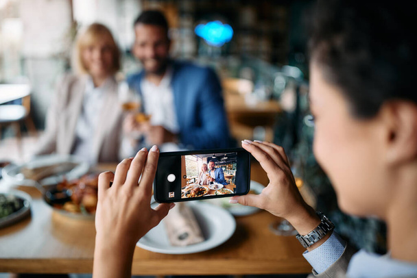 Close-up of entrepreneur using smart phone and taking picture of her colleagues while having business lunch in restaurant.  - Foto, Bild