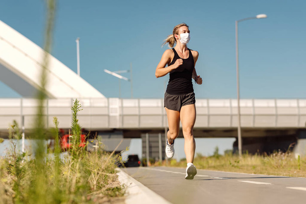 Young sportswoman wearing face  mask while jogging outdoors during coronavirus epidemic.  - Φωτογραφία, εικόνα