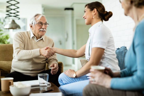 Happy mature man shaking hands with female nurse who is visiting him at home.  - Photo, Image