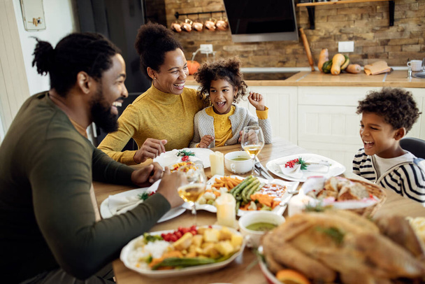 Szczęśliwa Afroamerykańska rodzina rozmawiająca i bawiąca się podczas obiadu w jadalni. Skupiamy się na matce i córce..  - Zdjęcie, obraz
