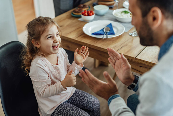 Cheerful small girl and her father playing clapping game and having fun in dining room.  - Foto, Imagen