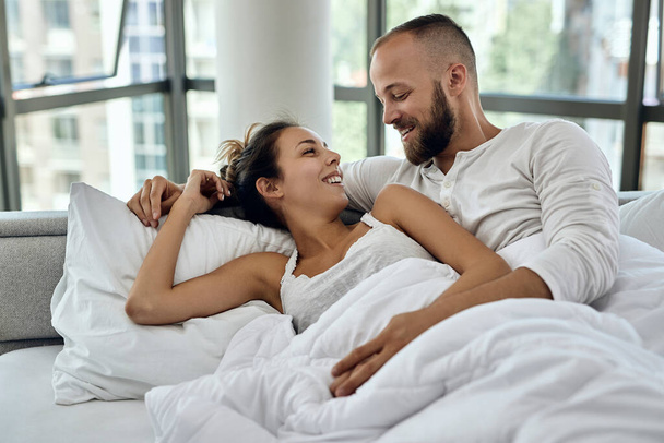 Счастливая влюбленная пара отдыхает на кровати и разговаривает друг с другом по утрам.  - Фото, изображение