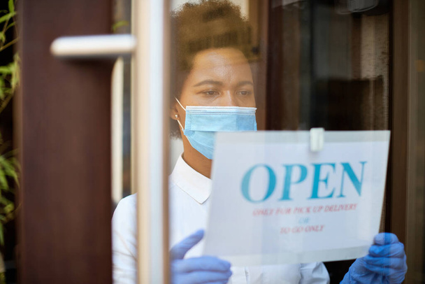 African American waitress hanging open sign while reopening restaurant for delivery and takeaway only during coronavirus epidemic.  - Valokuva, kuva