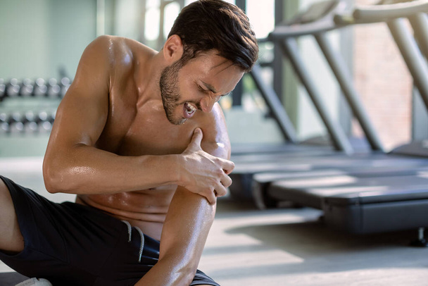 Young athletic man feeling pain in his shoulder while exercising in health club.  - 写真・画像
