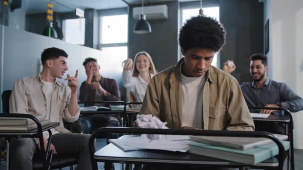 Unhappy african american student loser feeling mocking bullying anger from classmates suffering from abuse young upset distressed guy sits alone in classroom at desk discrimination and racism concept - Imágenes, Vídeo