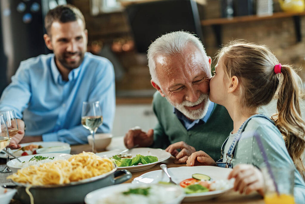 Любляча маленька дівчинка цілує свого дідуся під час сімейного обіду в їдальні
.  - Фото, зображення