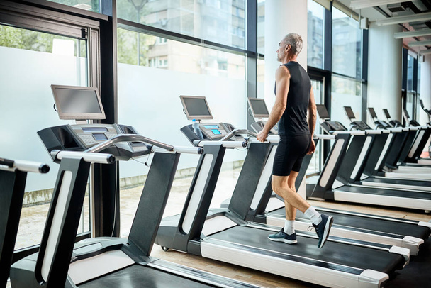 Mature athlete warming up for sports training and walking on treadmill in a gym.  - 写真・画像
