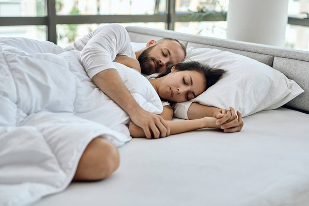 Молодая любящая пара лежала обнявшись, пока спала на кровати.  - Фото, изображение