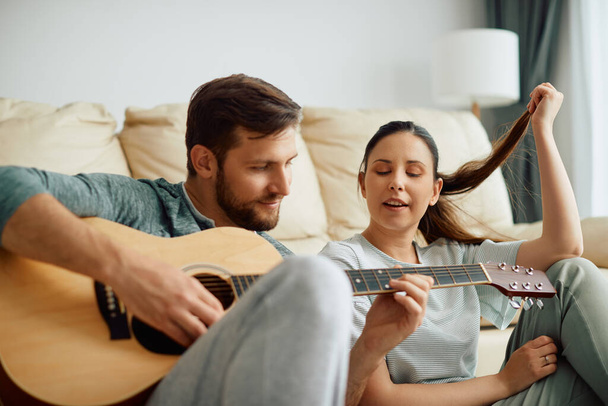 Smiling man playing acoustic guitar while his wife is singing. Focus is on woman.  - Foto, Imagem