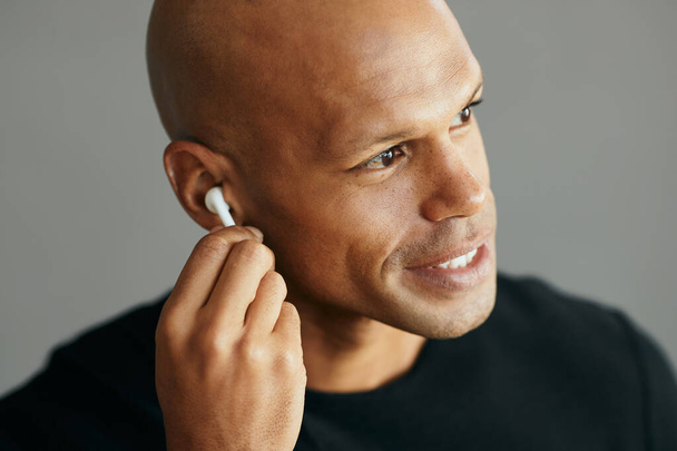 Young African American man using wireless in-ear headphones while listening music. - Foto, Imagem