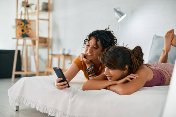 Young lesbian woman and her girlfriend using mobile phone while lying down on bed.  - Foto, Imagen