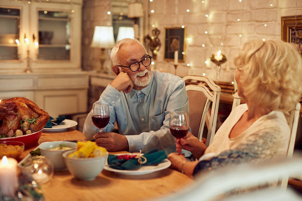Ο ευτυχισμένος ηλικιωμένος άντρας και η γυναίκα του μιλάνε πίνοντας κρασί στο τραπέζι των Ευχαριστιών..  - Φωτογραφία, εικόνα
