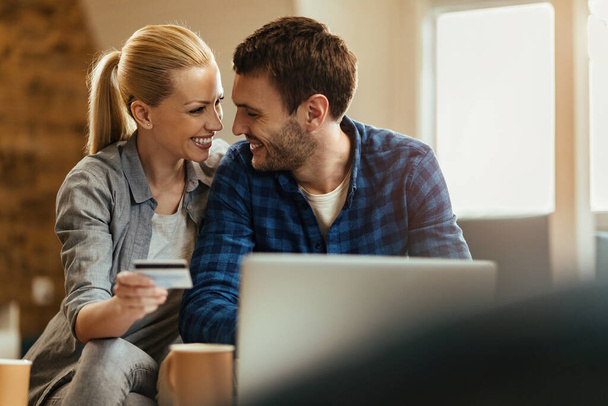 Ευτυχές ζευγάρι επικοινωνεί χρησιμοποιώντας πιστωτική κάρτα και laptop για online αγορές στο σπίτι. - Φωτογραφία, εικόνα