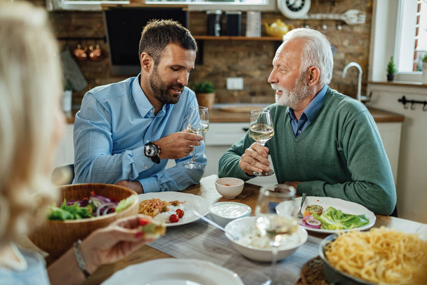 Młody człowiek i jego starszy ojciec piją wino i komunikują się podczas lunchu przy stole..  - Zdjęcie, obraz