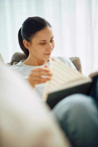 Young woman enjoying in reading a book while relaxing at home.  - 写真・画像