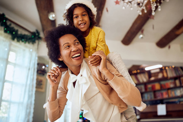 Carefree black mother and daughter having fun while piggybacking at home on Christmas day. - Fotoğraf, Görsel