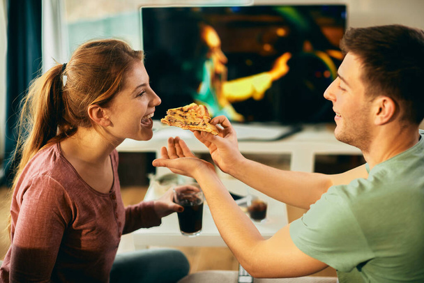 Happy woman having fun while boyfriend is feeding her pith pizza at home.  - Foto, Imagem