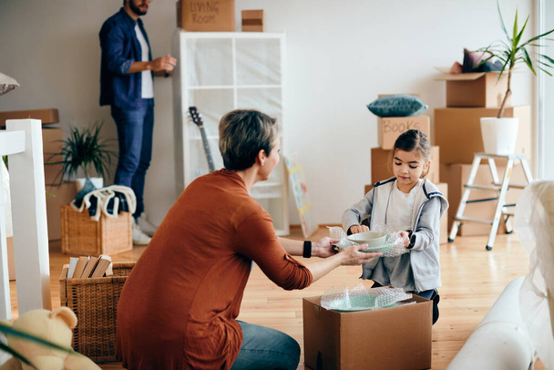 Small girl and her mother unpacking their belongings while moving into a new home. Father is i the background.  - Photo, Image