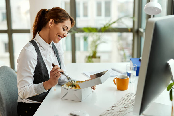 Young smiling businesswoman eating at her office desk. - Foto, imagen