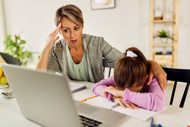 Little girl feeling sad while online learning and homeschooling with her mother.  - Foto, Imagen