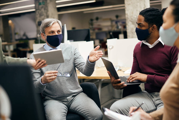Середній дорослий підприємець розмовляє зі своєю діловою командою під час зустрічі n офісу. Вони носять захисні маски для обличчя через пандемію коронавірусу
.  - Фото, зображення