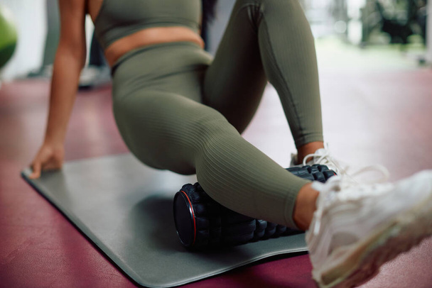 Close-up of athlete massaging her leg with foam roller in a gym. - Photo, Image