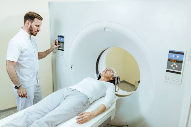 Senior female patient having CT scan examination while radiologist is supervising the procedure.  - Foto, Bild