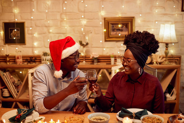 Happy African American couple having fun and toasting while eating at dining table on Christmas. - Фото, изображение