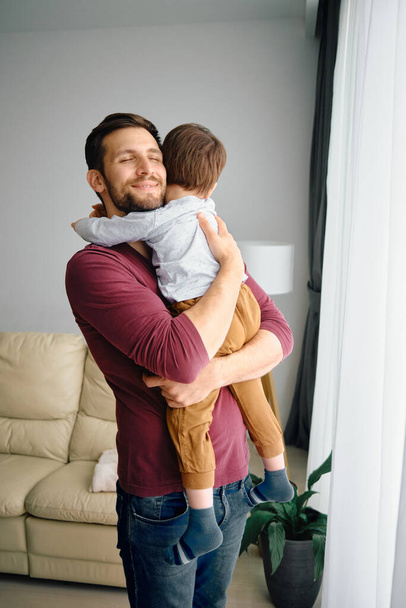 Young father enjoying with his son and embracing him at home. - Photo, image