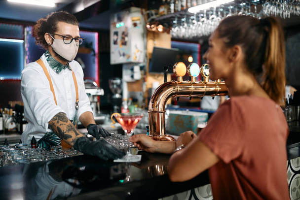 Щасливий бармен з маскою для обличчя, що подає коктейль жінці за барною стійкою
. - Фото, зображення